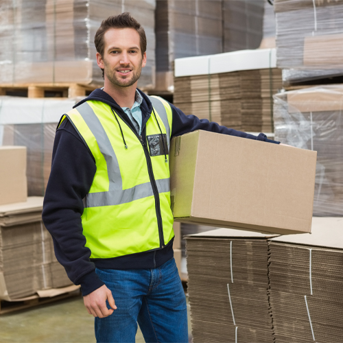 Man in warehouse holding cardboard box in front of pallet of cardboard boxes.
