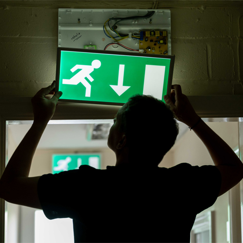Emergency lighting engineer lifting down an emergency light Emergency lighting engineer lifting down an emergency light