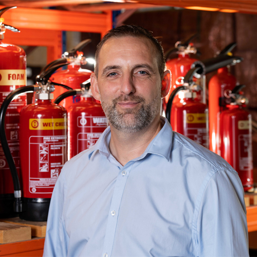 Neil from Right Action stood in front of some Fire Extinguishers