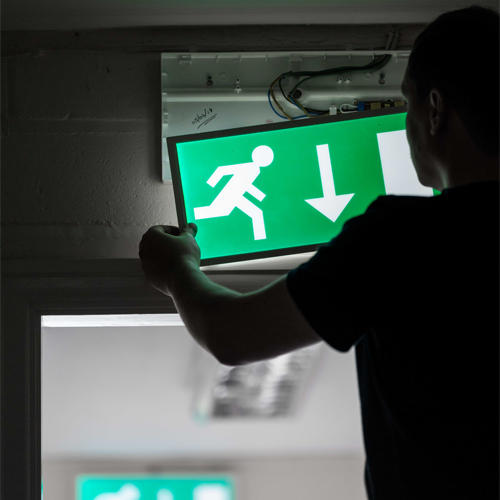 Emergency lighting engineer exposing wiring on an emergency light